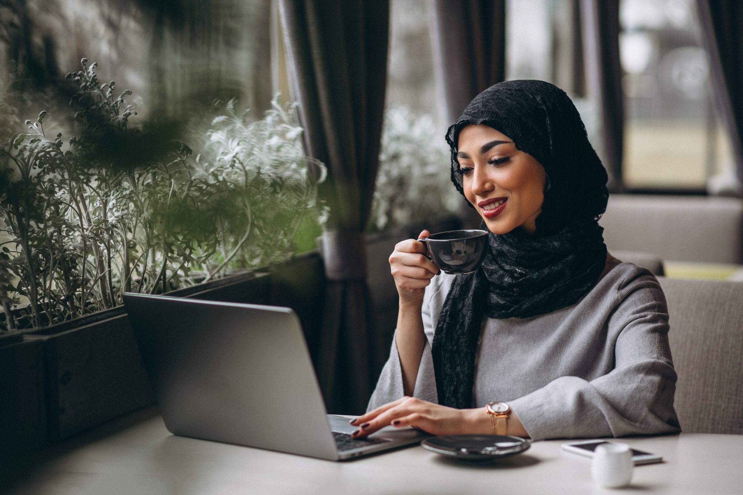 Arabian woman in hijab inside a cafe working on laptop